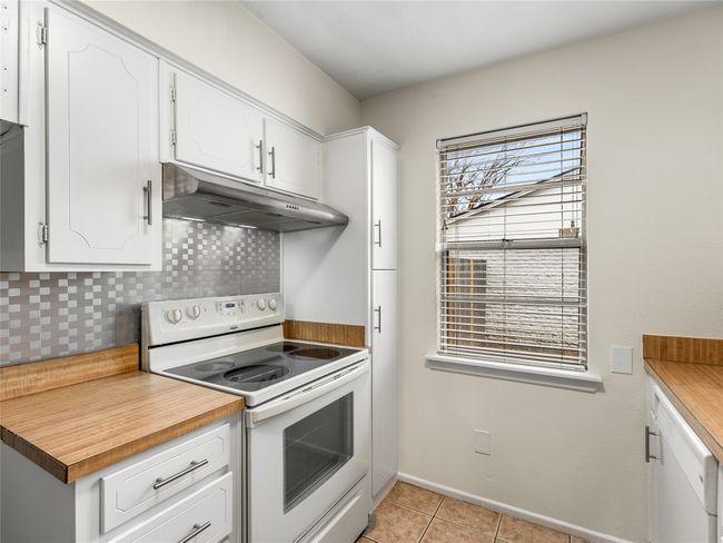 Kitchen with white cabinets, light tile patterned floors, electric range, and backsplash | Image 14