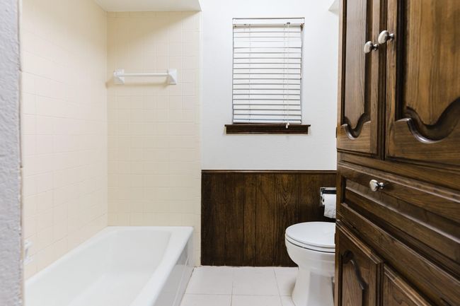 Full bath with wood walls, toilet, tile patterned floors, shower combination, and wainscoting | Image 21
