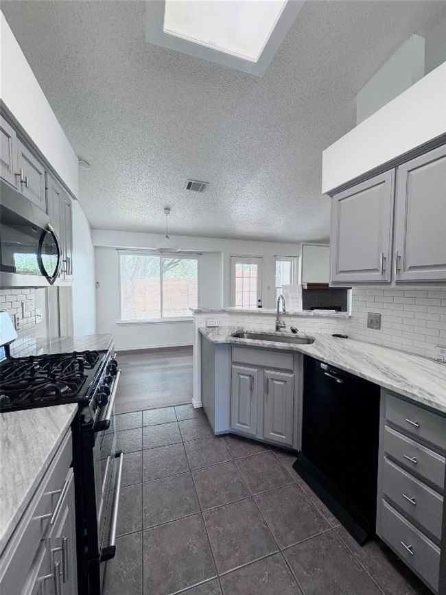 Kitchen with decorative backsplash, gray cabinets, black appliances, a textured ceiling, and a peninsula | Image 12