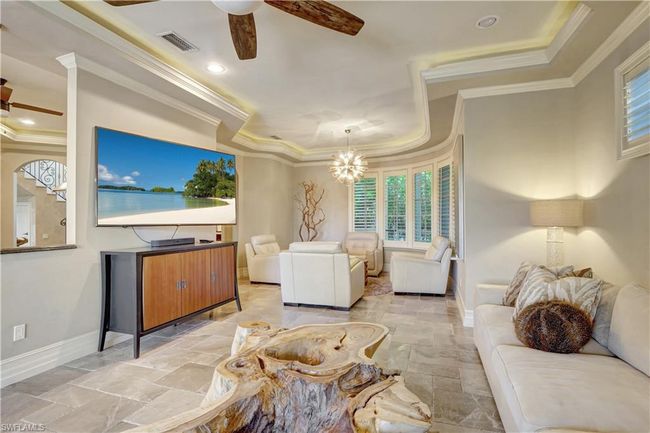 Living area featuring ceiling fan with notable chandelier, baseboards, visible vents, a raised ceiling, and crown molding | Image 22