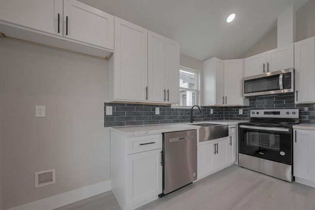 Well-appointed kitchen boasts abundant white cabinetry, generous counter space, a rich contrasting backsplash, and efficient layout suited for both cooking and hosting. | Image 11