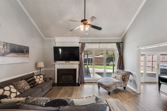 Living area featuring a textured ceiling, a ceiling fan, wood finished floors, a tiled fireplace, and ornamental molding | Image 8