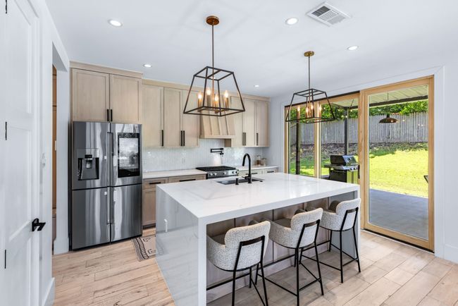 Kitchen with stainless steel refrigerator with ice dispenser, a chandelier, decorative backsplash, light stone counters, and light wood-style floors | Image 15