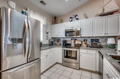 Kitchen with light stone countertops, light tile patterned floors, white cabinetry, and appliances with stainless steel finishes | Image 2