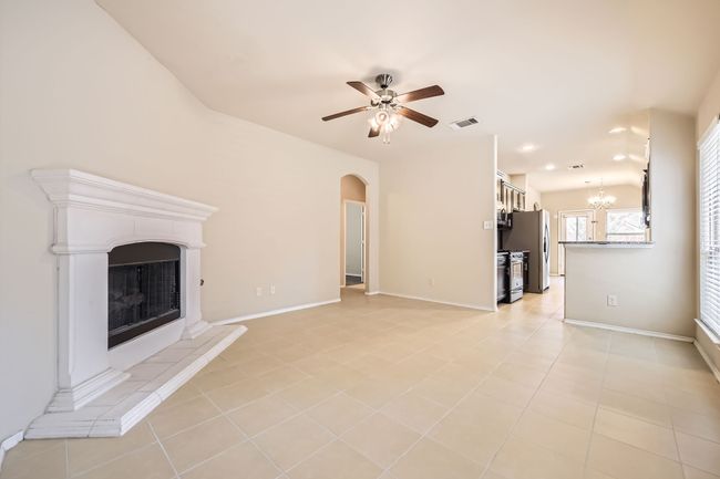Unfurnished living room featuring a ceiling fan, arched walkways, a fireplace with raised hearth, a chandelier, and light tile patterned flooring | Image 6