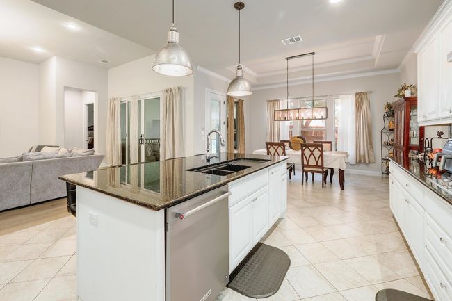 Kitchen featuring stainless steel dishwasher, a raised ceiling, a kitchen island with sink, light tile patterned floors, and dark stone counters | Image 13