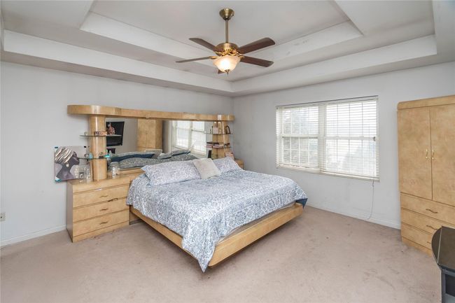 Bedroom with light colored carpet, a ceiling fan, a raised ceiling, and baseboards | Image 27