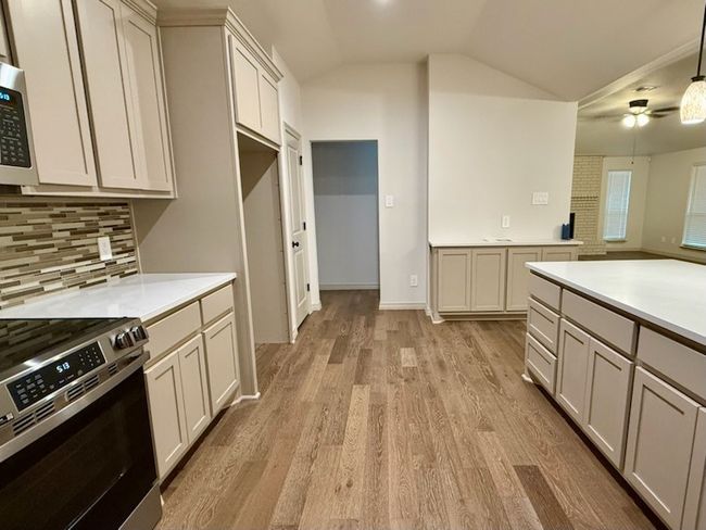 Kitchen featuring appliances with stainless steel finishes, light wood finished floors, lofted ceiling, decorative backsplash, and light countertops | Image 9