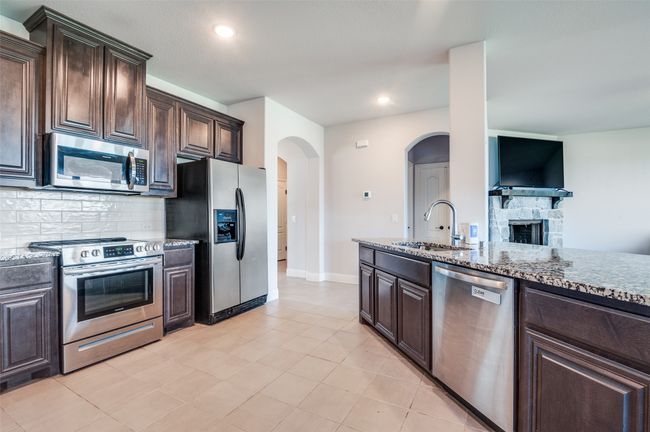 Kitchen with appliances with stainless steel finishes, decorative backsplash, dark brown cabinets, light stone counters, and recessed lighting | Image 9