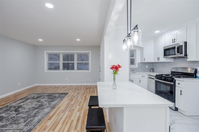 Kitchen featuring white cabinetry, appliances with stainless steel finishes, tasteful backsplash, pendant lighting, and light stone counters | Image 13