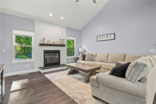 Living room with high vaulted ceiling, dark wood-type flooring, a large fireplace, and ceiling fan | Image 8