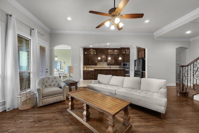 Living area with arched walkways, ceiling fan, dark wood-type flooring, stairs, and ornamental molding | Image 6