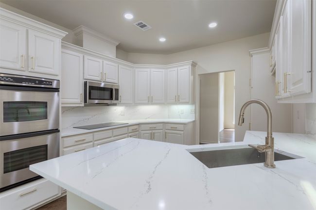 Kitchen with stainless steel appliances, a sink, white cabinetry, recessed lighting, and light stone counters | Image 14