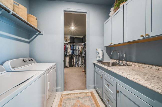 Laundry room has access from the primary bedroom and features sink with upgraded cabinet colors and shelving. | Image 21