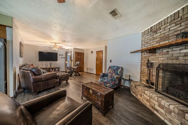 Living area with a ceiling fan, wood finished floors, a textured ceiling, and a brick fireplace | Image 10