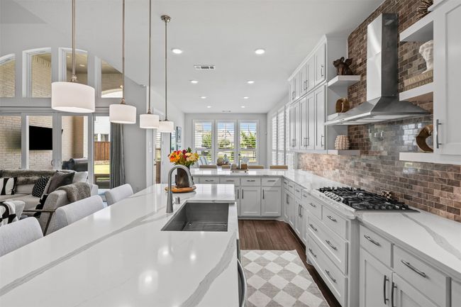 Kitchen featuring wall chimney range hood, a sink, open floor plan, stainless steel gas cooktop, and decorative backsplash | Image 16