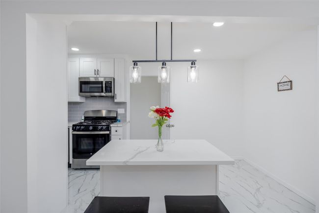 Kitchen featuring backsplash, hanging light fixtures, white cabinets, range with gas stovetop, and light stone counters | Image 14