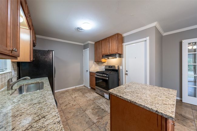 Kitchen featuring stainless steel range with gas cooktop, under cabinet range hood, tasteful backsplash, brown cabinetry, and ornamental molding | Image 10