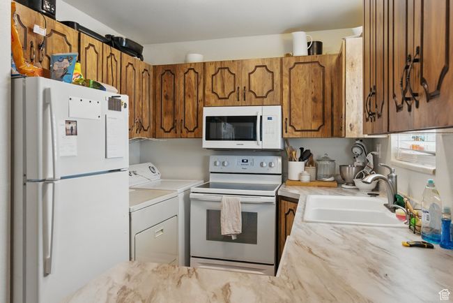 Kitchen with light countertops, a sink, washing machine and dryer, white appliances, and brown cabinetry | Image 9