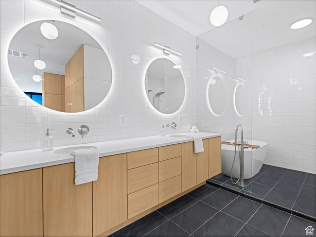 Full bathroom featuring a freestanding tub, double vanity, tile patterned flooring, tile walls, and a sink | Image 22