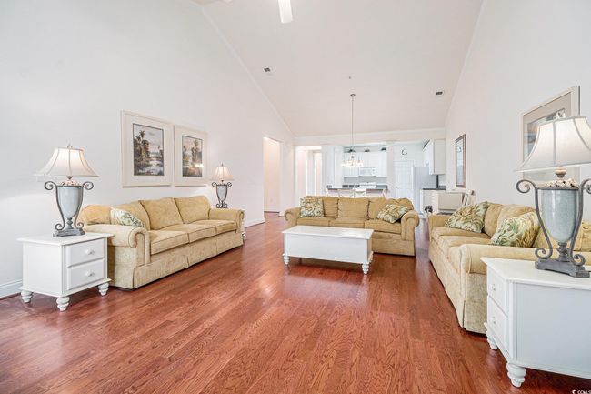Living area with high vaulted ceiling, wood finished floors, a chandelier, and baseboards | Image 7