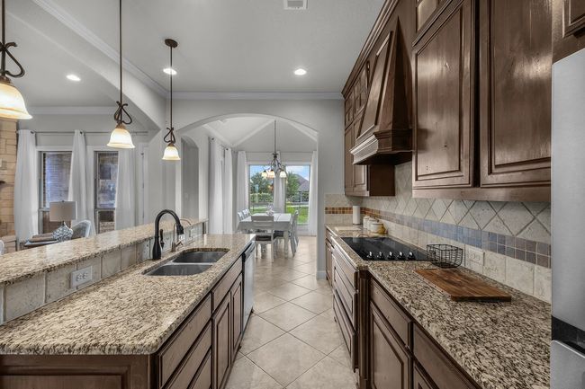 Kitchen featuring arched walkways, a sink, tasteful backsplash, black electric stovetop, and light stone counters | Image 19