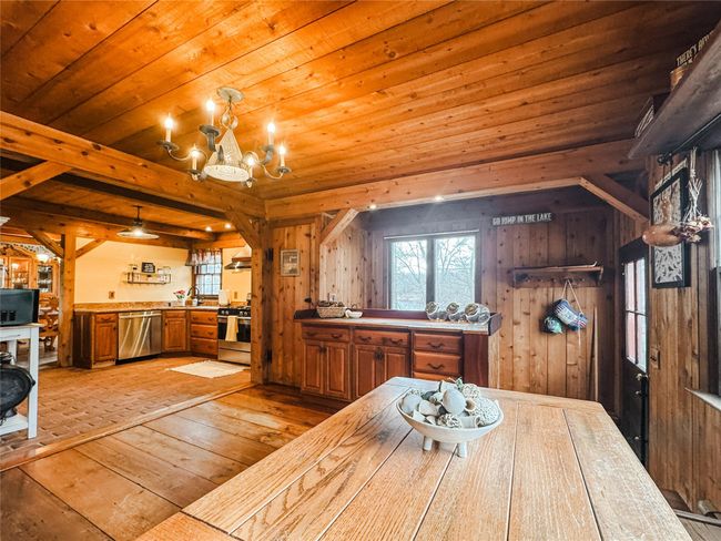 Dining room featuring wooden walls, wooden ceiling, beamed ceiling, an inviting chandelier, and light wood-type flooring | Image 14