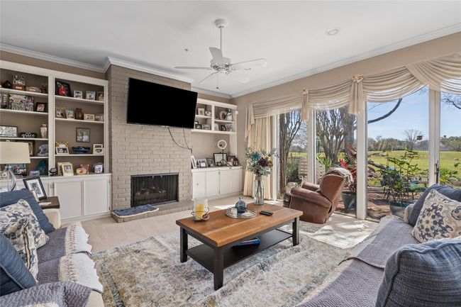 This inviting living space boasts a beautiful brick fireplace, flanked by built-in shelving for storage and display. Floor-to-ceiling windows provide breathtaking views of the lush golf course, filling the room with natural light. The neutral tones and crown molding add a touch of elegance, while the open layout makes it a perfect gathering spot. | Image 11