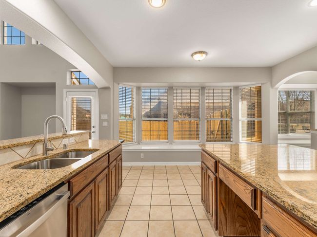 Kitchen with light tile patterned floors, brown cabinetry, baseboards, a sink, and stainless steel dishwasher | Image 14