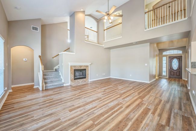 Unfurnished living room featuring a high ceiling, visible vents, light wood-style floors, baseboards, and ceiling fan | Image 7