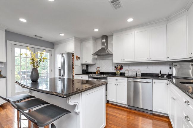 Kitchen with wall chimney exhaust hood, a kitchen bar, visible vents, hardwood / wood-style floors, and stainless steel appliances | Image 5