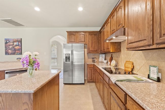Kitchen featuring stainless steel appliances, under cabinet range hood, arched walkways, brown cabinets, and backsplash | Image 10
