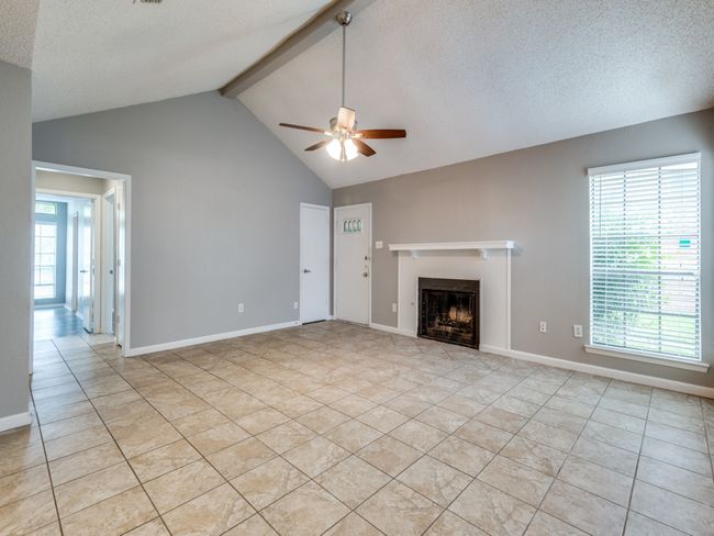Unfurnished living room with ceiling fan, a fireplace, light tile patterned floors, beam ceiling, and high vaulted ceiling | Image 4