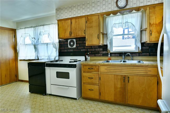 Kitchen featuring tile counters, light floors, white range with electric stovetop, a sink, and black dishwasher | Image 18
