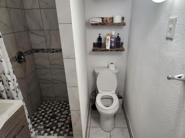 Modern bathroom in a two-bedroom unit featuring a stylish tiled shower and convenient shelving for storage. | Image 11