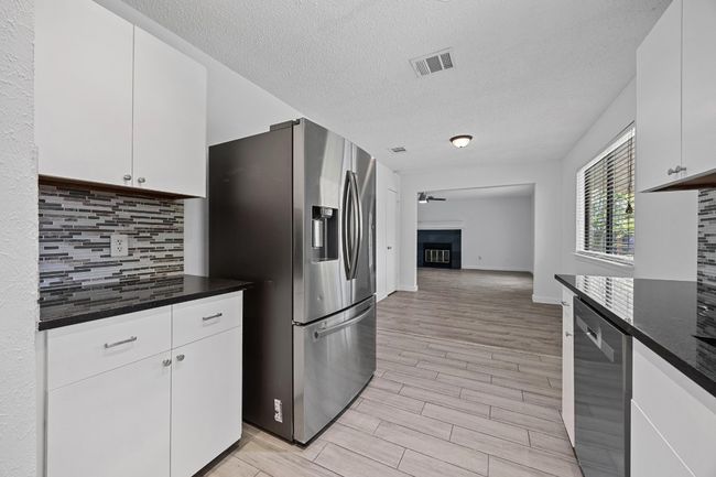 Kitchen with light wood finished floors, stainless steel appliances, a textured ceiling, white cabinetry, and decorative backsplash | Image 12