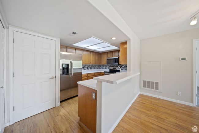 Kitchen with appliances with stainless steel finishes, light wood-type flooring, brown cabinetry, a peninsula, and recessed lighting | Image 5