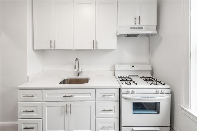 Kitchen with white gas range, white cabinetry, under cabinet range hood, and a sink | Image 5