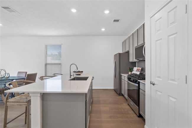 This spacious kitchen features high ceilings, stained wood cabinets, Silestone countertops, SS appliances, modern tile backsplash, recessed lighting, huge kitchen island with single sink and space for breakfast bar, and a pantry all overlooking your huge family room. | Image 11