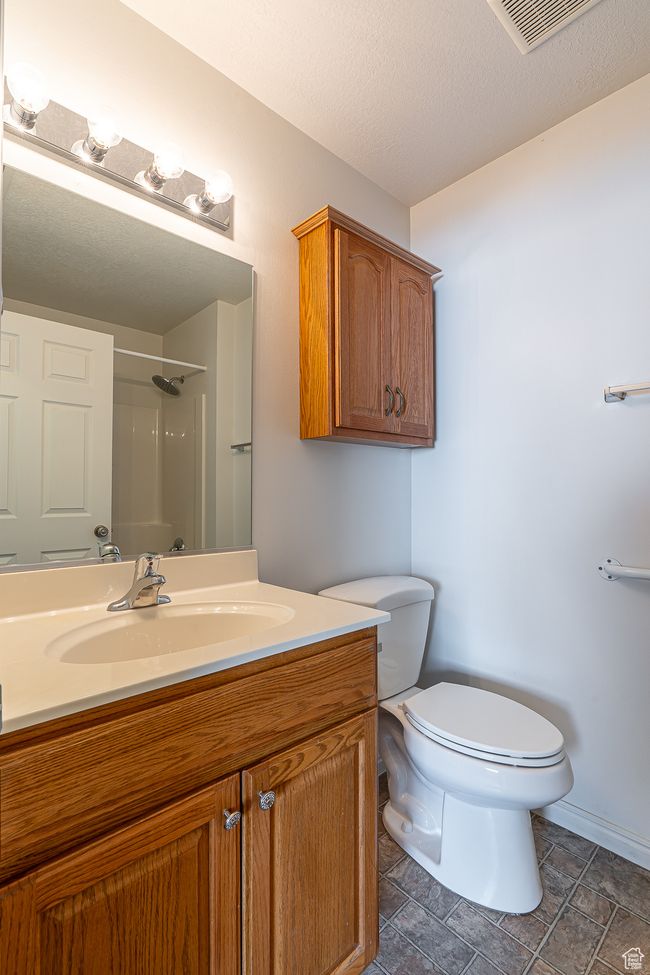 Full bath featuring a textured ceiling, visible vents, a shower, toilet, and vanity | Image 23