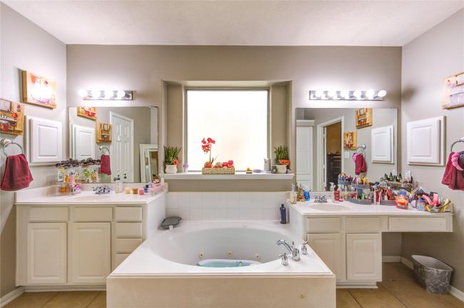 This spacious bathroom features a central jacuzzi bathtub, dual sinks with ample counter space, and large mirrors for a bright and open feel. The neutral color palette and recessed window add elegance, while the overhead lighting provides functionality. | Image 22