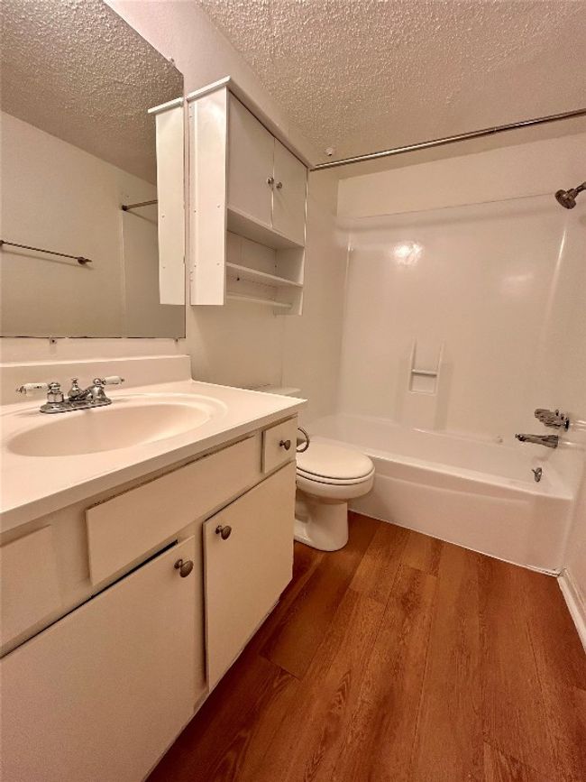 Full bathroom featuring a textured ceiling, wood finished floors, vanity, and shower / bathtub combination | Image 5