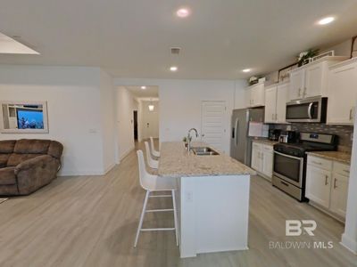 Kitchen with stainless steel appliances, white cabinets, decorative backsplash, sink, and light hardwood / wood-style flooring | Image 3