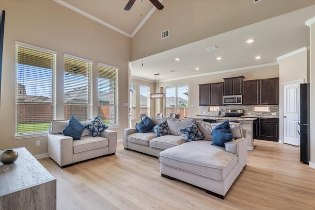 Living room with ornamental molding, light wood finished floors, a ceiling fan, baseboards, and high vaulted ceiling | Image 14