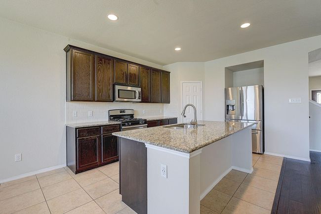 Kitchen featuring appliances with stainless steel finishes, a sink, light stone countertops, dark brown cabinetry, and a kitchen island with sink | Image 4