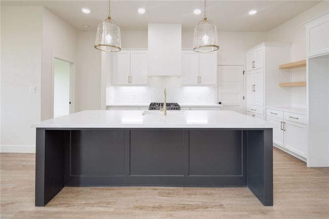 Kitchen featuring a large island with sink, tasteful backsplash, light countertops, white cabinetry, and decorative light fixtures | Image 9