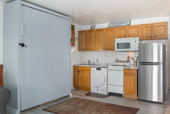 Kitchen featuring white appliances, washer / dryer, light wood finished floors, light stone countertops, and brown cabinets | Image 10