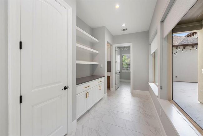 This bright and functional mudroom hallway features sleek open shelving, chic gold hardware, and a large window overlooking the courtyard—blending style and storage in one streamlined space. | Image 18
