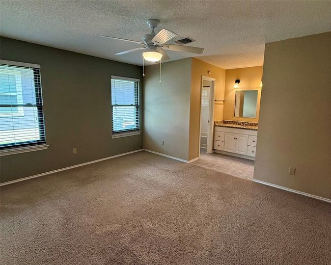 Unfurnished bedroom with light colored carpet, baseboards, a textured ceiling, ensuite bath, and a ceiling fan | Image 13
