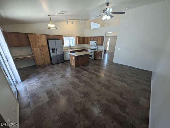 Kitchen featuring stone tile flooring, ceiling fan, white appliances, a center island, and light countertops | Image 5